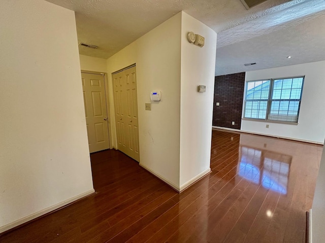 corridor with visible vents, dark wood-style flooring, and a textured ceiling