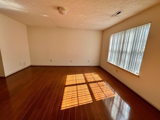 spare room with visible vents, a textured ceiling, baseboards, and hardwood / wood-style flooring