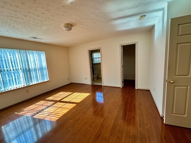 unfurnished room with visible vents, a textured ceiling, baseboards, and wood finished floors