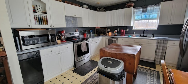 kitchen featuring a sink, appliances with stainless steel finishes, white cabinets, glass insert cabinets, and light floors