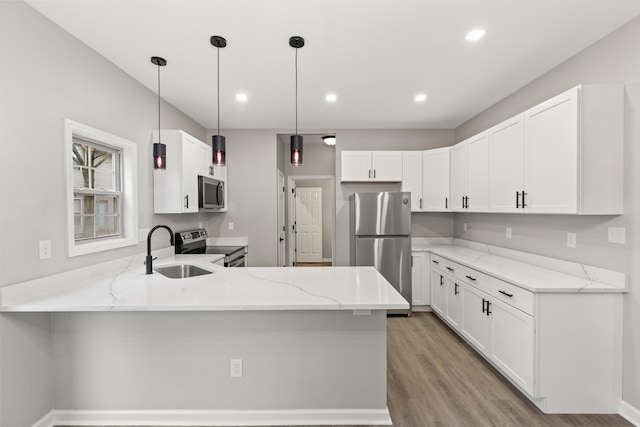 kitchen with a sink, light stone counters, appliances with stainless steel finishes, and a peninsula