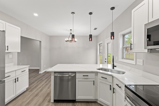 kitchen featuring light stone countertops, a peninsula, a sink, white cabinets, and appliances with stainless steel finishes