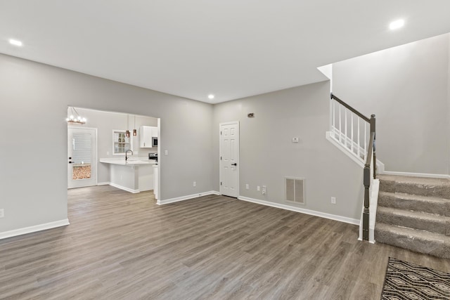 unfurnished living room featuring stairs, light wood-style flooring, baseboards, and visible vents