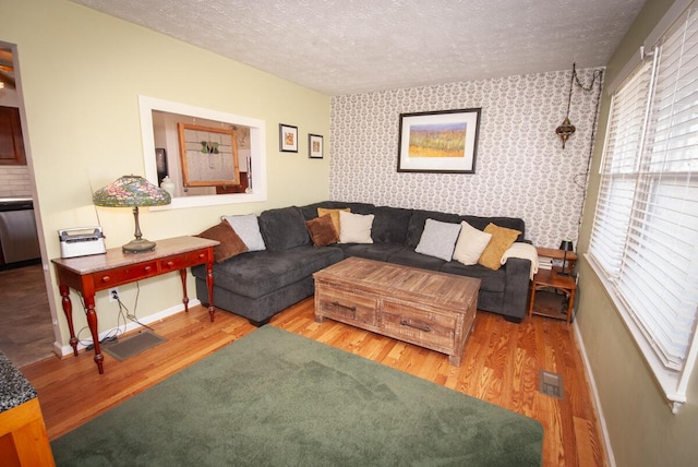 living area with baseboards, a textured ceiling, wood finished floors, and wallpapered walls