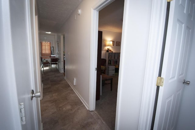 hallway featuring a textured ceiling and baseboards