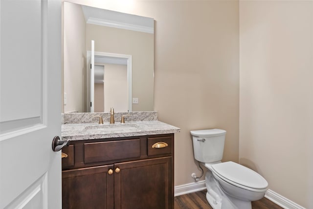 bathroom with toilet, wood finished floors, crown molding, baseboards, and vanity