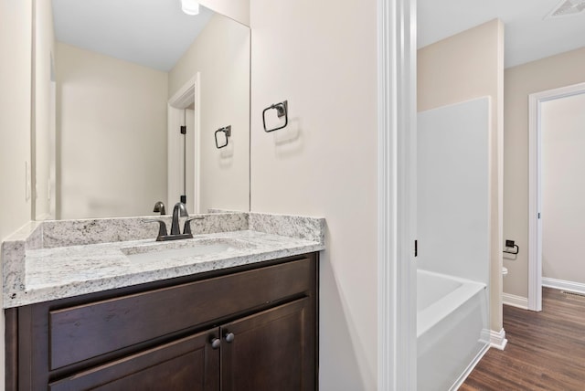 bathroom featuring visible vents, baseboards, wood finished floors, a bath, and vanity