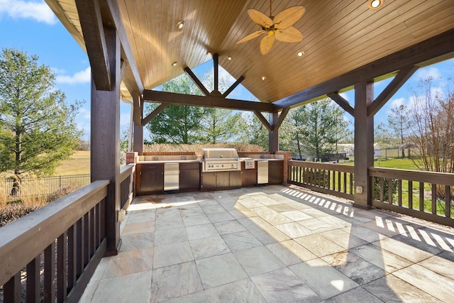 view of patio featuring fence, a gazebo, area for grilling, an outdoor kitchen, and a ceiling fan