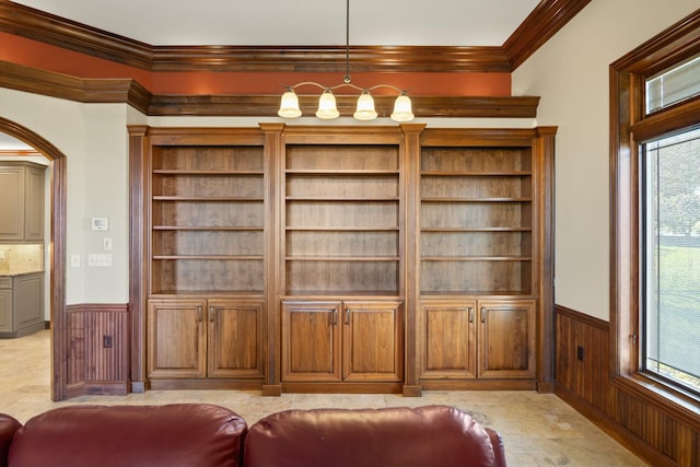 interior space featuring a chandelier, wooden walls, wainscoting, and crown molding