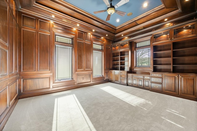 carpeted empty room with wooden walls, built in shelves, ornamental molding, a decorative wall, and a ceiling fan