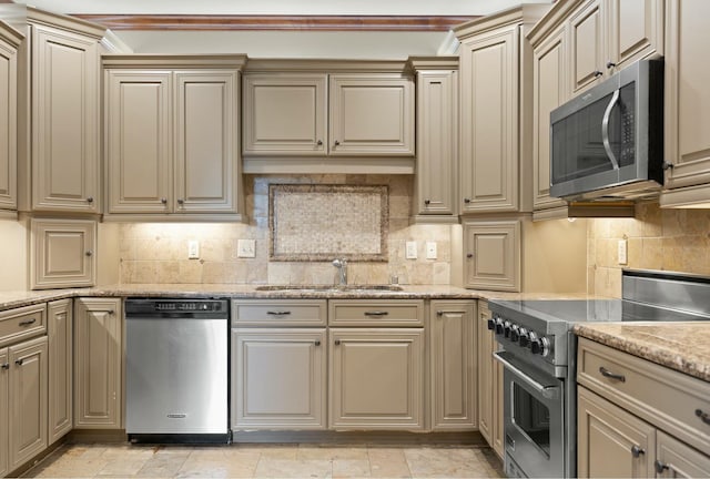 kitchen with light stone counters, a sink, appliances with stainless steel finishes, cream cabinets, and tasteful backsplash