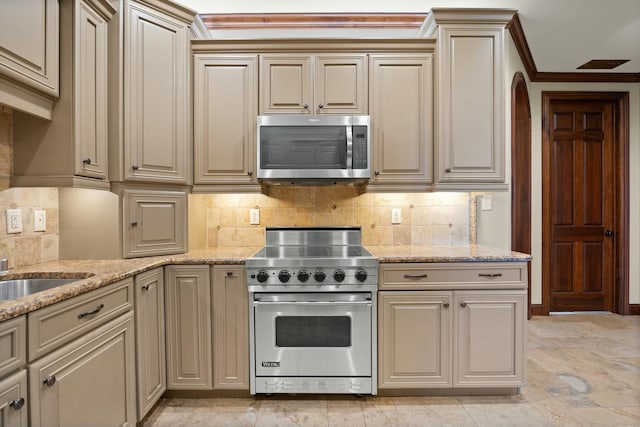 kitchen with light stone counters, cream cabinetry, appliances with stainless steel finishes, and ornamental molding