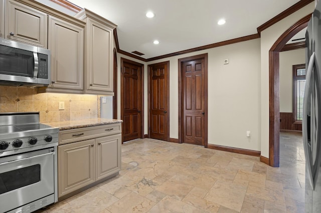 kitchen featuring cream cabinetry, tasteful backsplash, arched walkways, appliances with stainless steel finishes, and crown molding