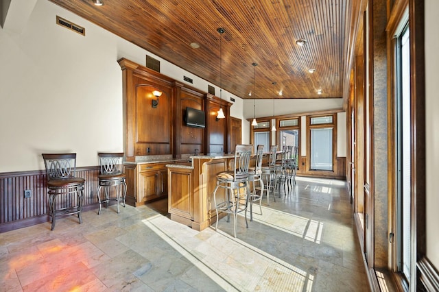 kitchen featuring a wainscoted wall, visible vents, a breakfast bar, vaulted ceiling, and wooden ceiling