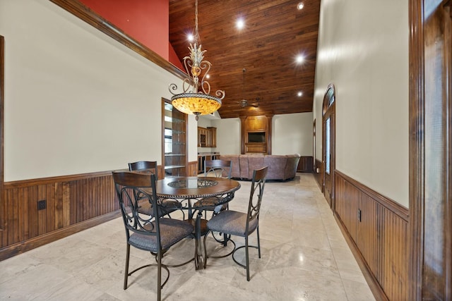 dining space with a wainscoted wall, high vaulted ceiling, an inviting chandelier, wooden ceiling, and wood walls