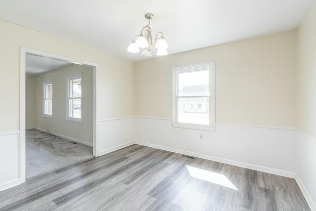 unfurnished room with a wealth of natural light, visible vents, an inviting chandelier, and wood finished floors