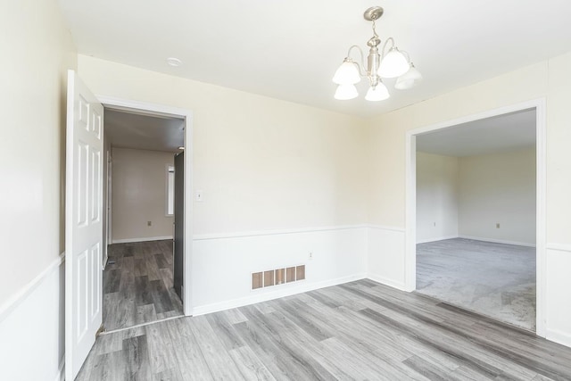 spare room featuring a notable chandelier, wood finished floors, visible vents, and baseboards