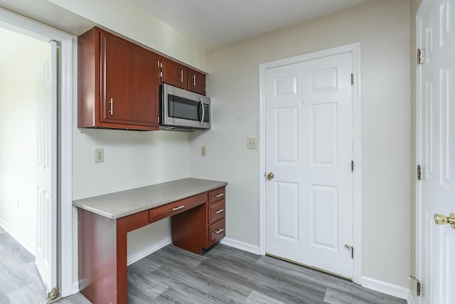 kitchen with stainless steel microwave, built in study area, light countertops, and wood finished floors