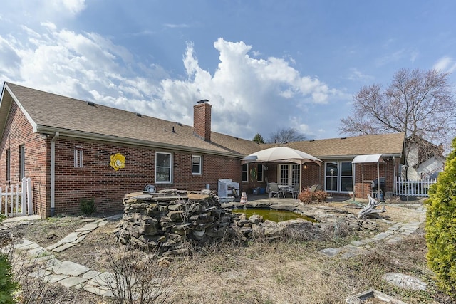 rear view of house with fence, a patio area, brick siding, and a chimney