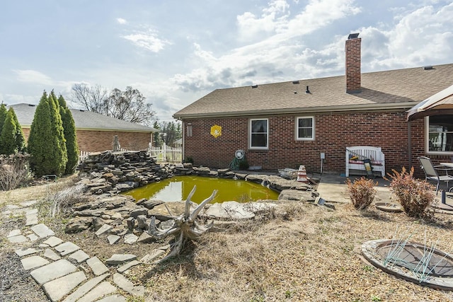 back of property with brick siding, a patio area, a chimney, and a garden pond