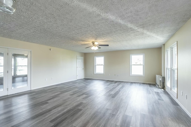 empty room with dark wood finished floors, a textured ceiling, baseboards, and ceiling fan