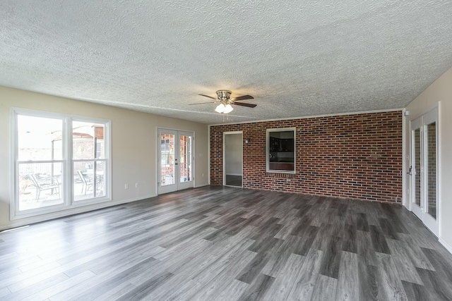 unfurnished living room with brick wall, dark wood finished floors, ceiling fan, french doors, and a textured ceiling