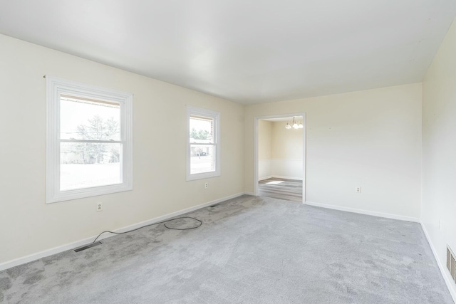 spare room featuring an inviting chandelier, baseboards, visible vents, and light carpet