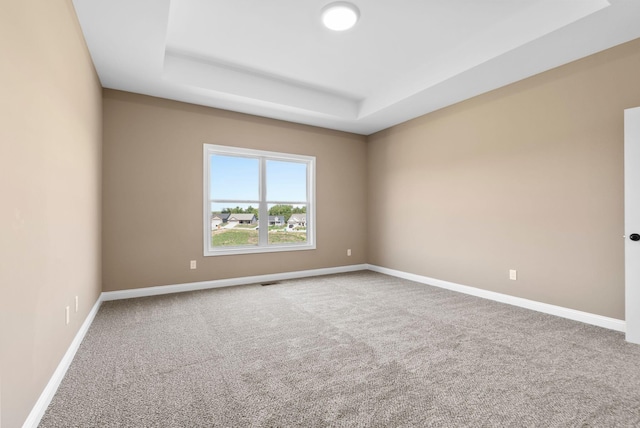 carpeted spare room with a tray ceiling and baseboards