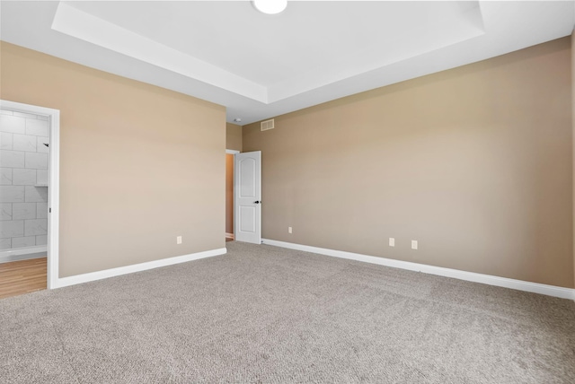 empty room featuring a tray ceiling, carpet, visible vents, and baseboards