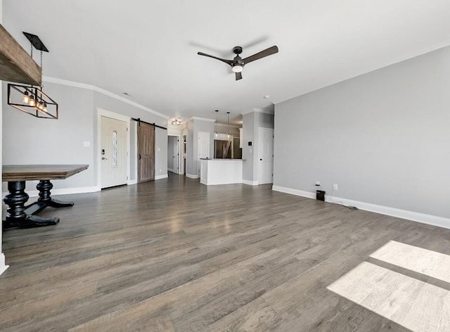 unfurnished living room featuring baseboards, ornamental molding, dark wood-type flooring, a barn door, and ceiling fan with notable chandelier