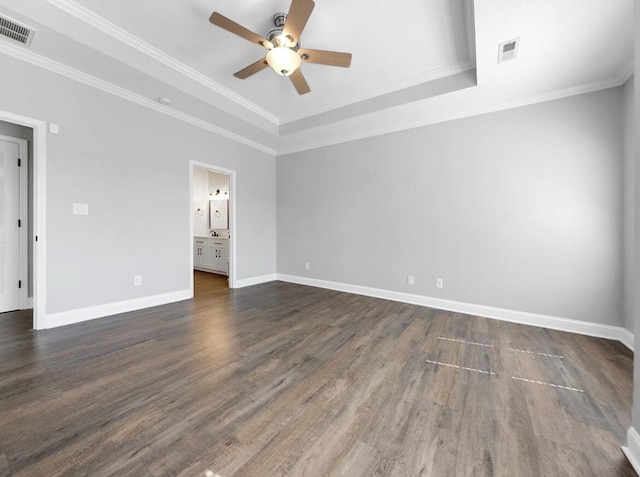 unfurnished bedroom featuring visible vents, crown molding, baseboards, a tray ceiling, and dark wood-style flooring