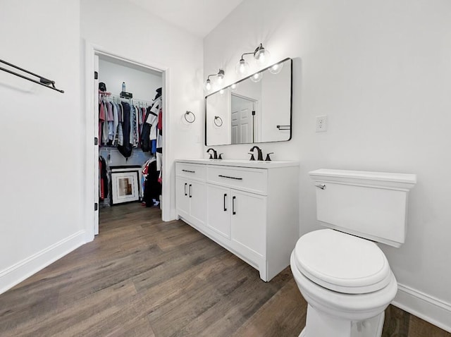 bathroom featuring double vanity, toilet, wood finished floors, and baseboards