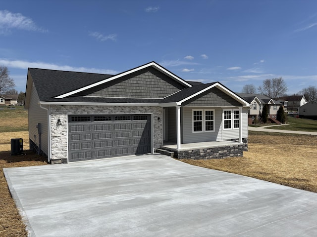 view of front facade featuring cooling unit, an attached garage, covered porch, concrete driveway, and stone siding