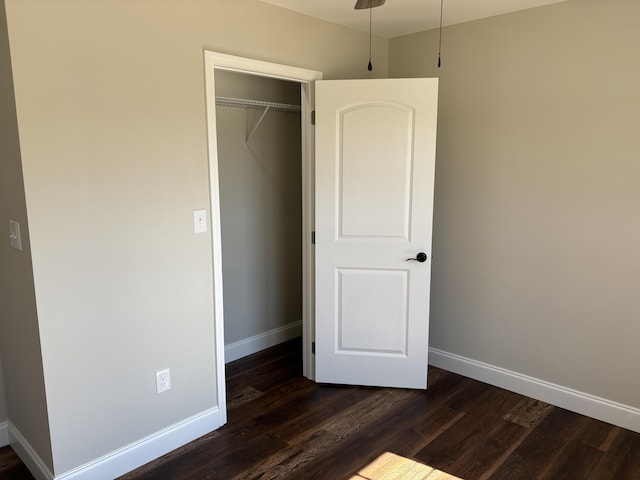 unfurnished bedroom with dark wood finished floors, baseboards, and a closet