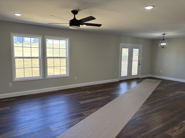 unfurnished living room with ceiling fan with notable chandelier, dark wood-style flooring, and baseboards