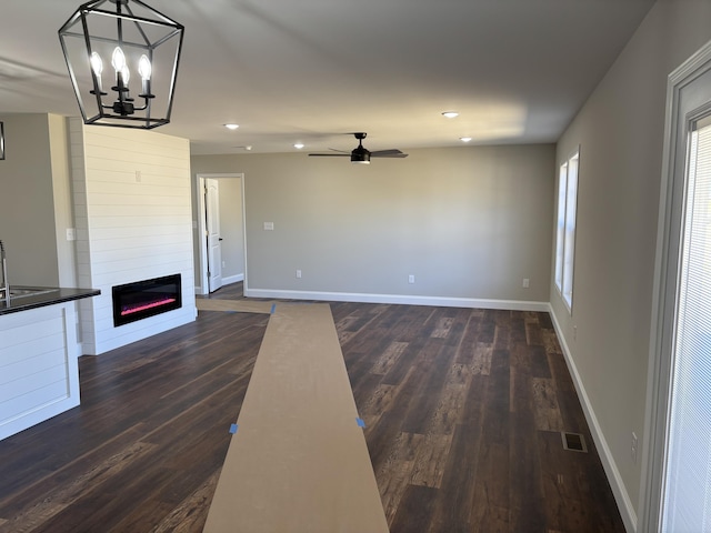 unfurnished living room with visible vents, dark wood-type flooring, ceiling fan with notable chandelier, a large fireplace, and baseboards