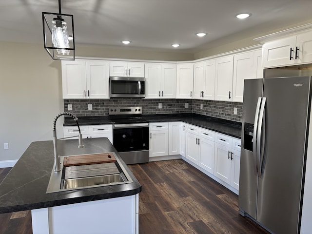 kitchen with dark countertops, a sink, a kitchen island, stainless steel appliances, and dark wood-style flooring