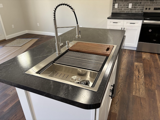 room details with stainless steel electric range, dark wood-style flooring, a sink, white cabinets, and dark countertops