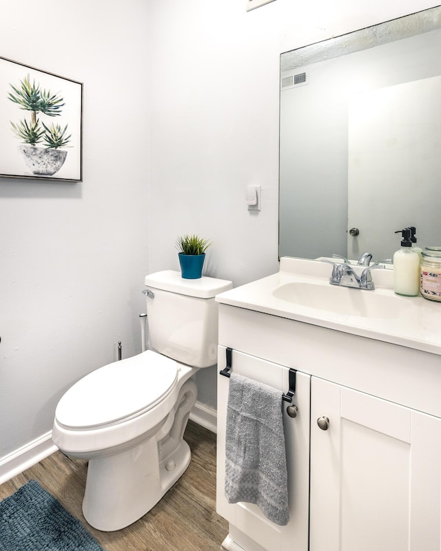 bathroom featuring visible vents, baseboards, toilet, wood finished floors, and vanity