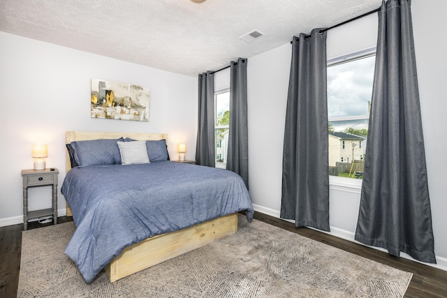 bedroom featuring visible vents, a textured ceiling, baseboards, and wood finished floors