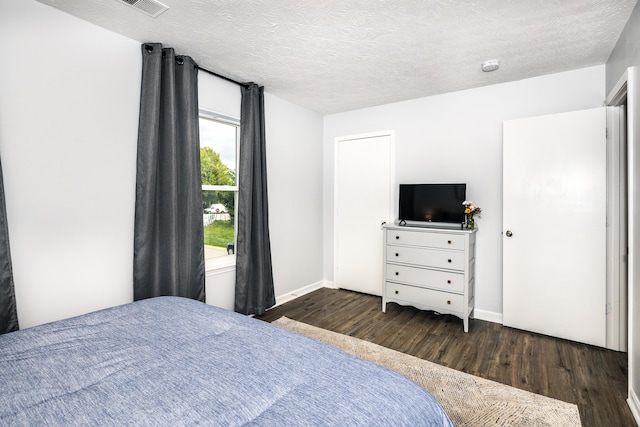 bedroom with visible vents, a textured ceiling, baseboards, and wood finished floors