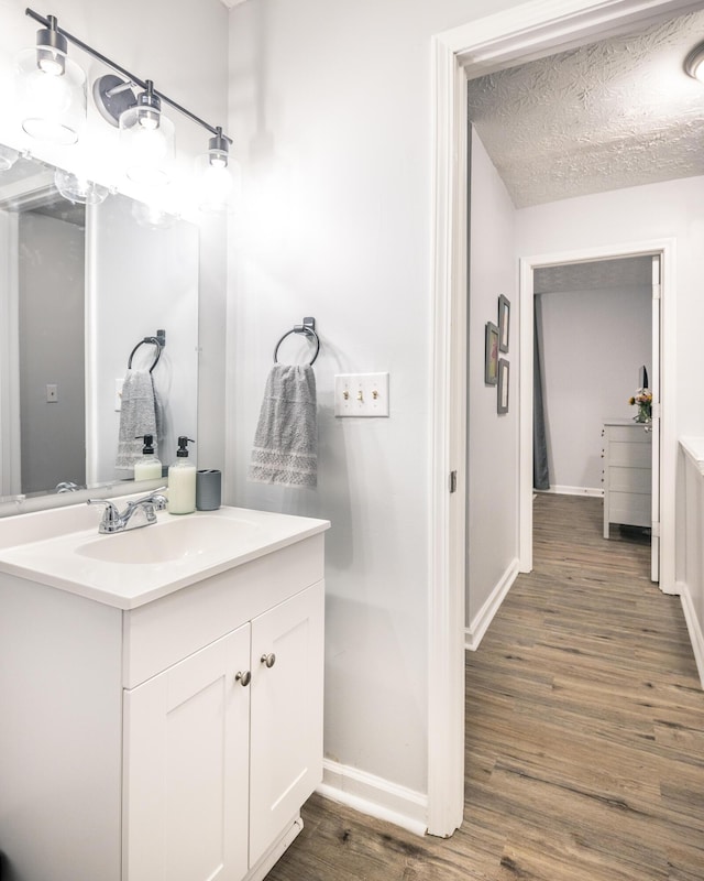 bathroom featuring a textured ceiling, vanity, baseboards, and wood finished floors