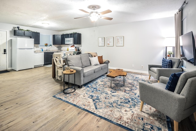 living area featuring ceiling fan, baseboards, light wood finished floors, and a textured ceiling