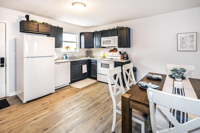 kitchen featuring white appliances, light wood finished floors, a sink, light countertops, and a textured ceiling