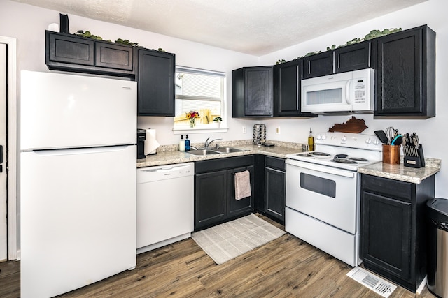 kitchen featuring dark cabinetry, white appliances, wood finished floors, visible vents, and a sink