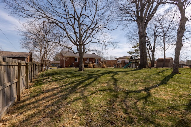 view of yard featuring a shed, a playground, an outdoor structure, and fence