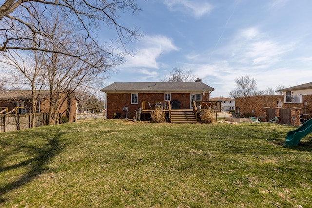 back of house with a lawn, a deck, a playground, fence, and brick siding