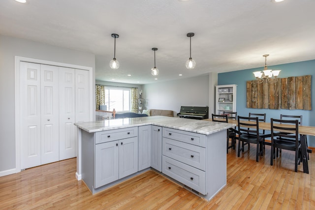 kitchen featuring light stone counters, gray cabinetry, hanging light fixtures, light wood-style floors, and a notable chandelier