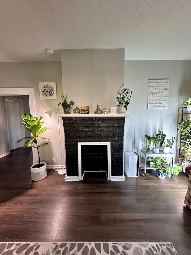 living area with baseboards, a textured ceiling, a brick fireplace, and wood finished floors