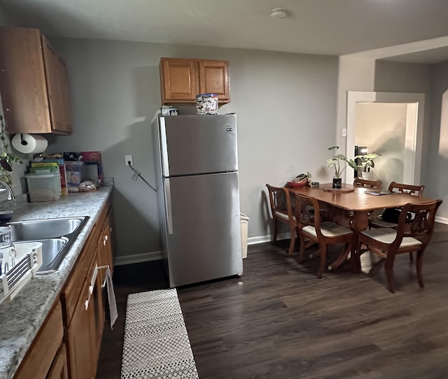 kitchen featuring dark wood-style floors, freestanding refrigerator, baseboards, and a sink